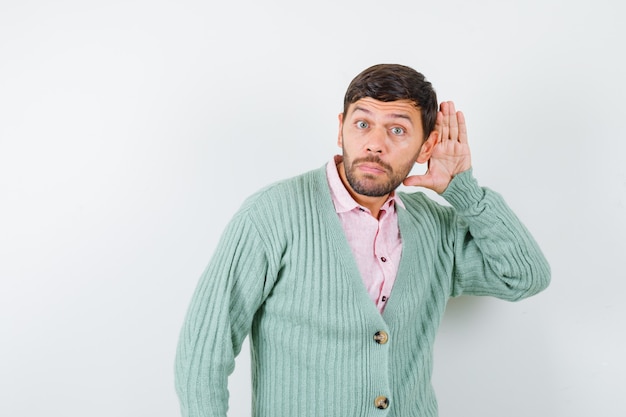 Free photo young male in shirt, cardigan with hand behind ear and looking focused , front view.