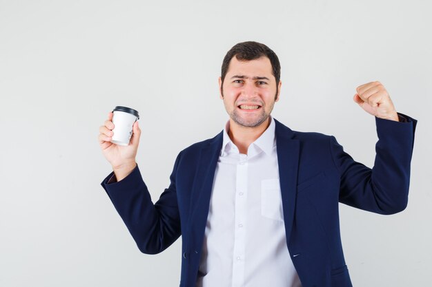 Young male in shirt, jacket holding cup of coffee and looking lucky