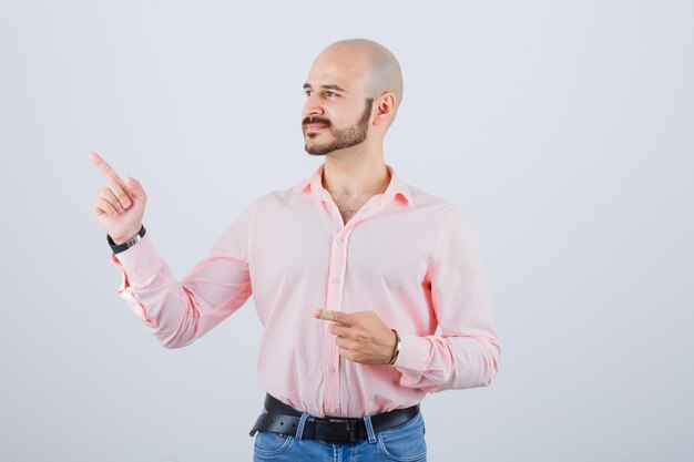 Young male in shirt, jeans pointing aside and looking happy , front view.