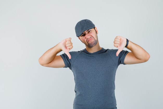 Free photo young male showing double thumbs down in grey t-shirt cap and looking disappointed