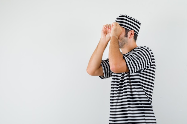 Free photo young male showing glasses gesture in t-shirt, hat and looking focused .