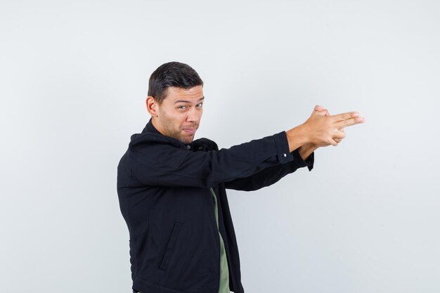 Young male showing gun gesture in t-shirt, jacket and looking irritated. front view.