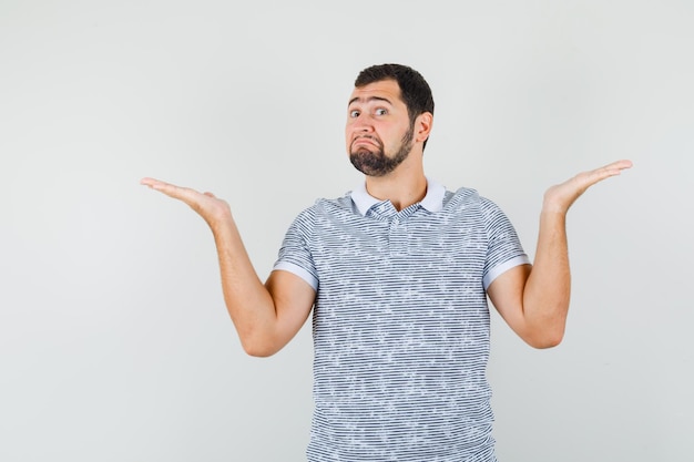 Young male showing helpless gesture in t-shirt and looking unaware. front view.