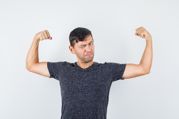 Young male showing his arm muscles in black t-shirt and looking strong , front view.