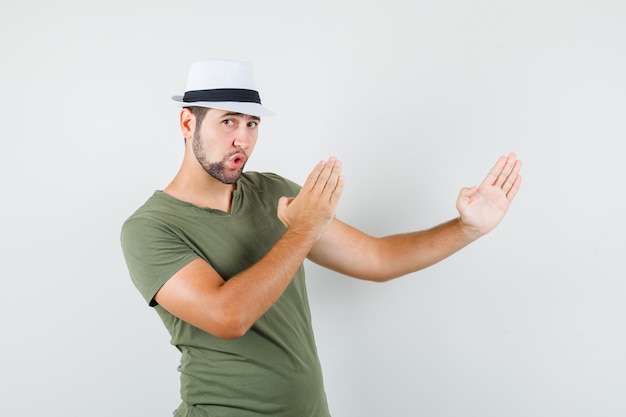 Young male showing karate chop gesture in green t-shirt and hat and looking strong