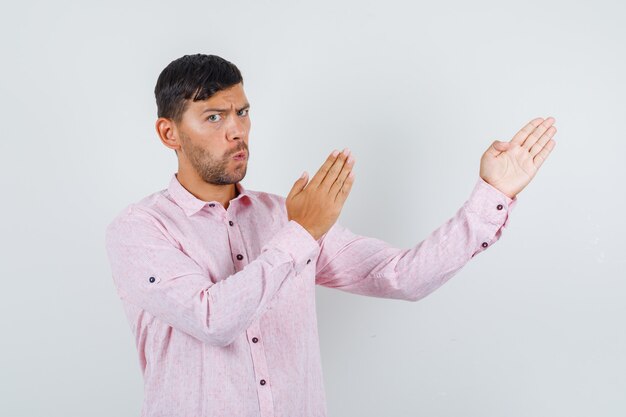 Young male showing karate chop gesture in pink shirt and looking serious , front view.