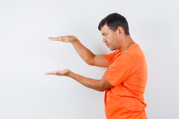 Young male showing size sign in orange t-shirt and looking sensible