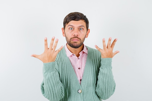 Young male showing ten fingers in shirt, cardigan and looking serious , front view.