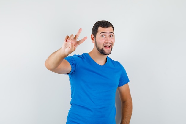 Young male showing victory sign in blue t-shirt and looking joyful