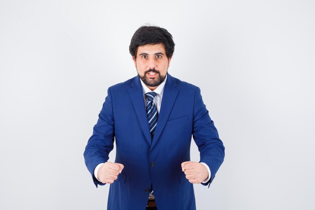 Young male showing winner gesture in shirt,jacket,tie and looking confident. front view.