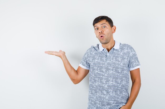 Young male spreading palm aside in t-shirt and looking surprised