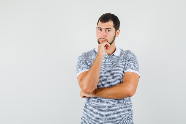 Young male standing in thinking pose in t-shirt and looking sensible , front view.