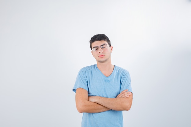 Young male standing with crossed arms in t-shirt and looking disappointed , front view.