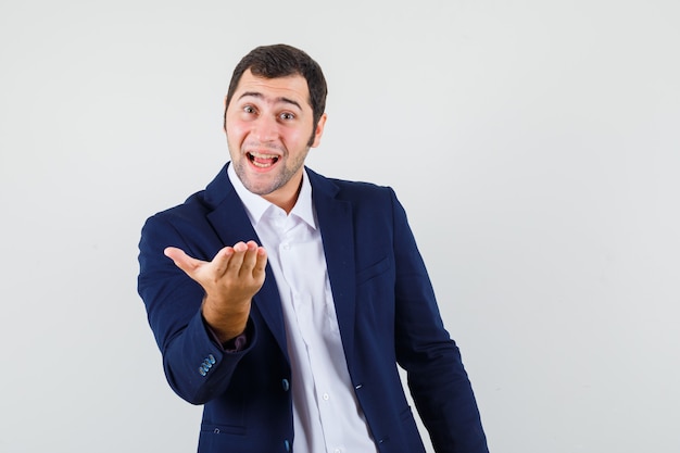 Young male stretching hand in questioning gesture in shirt, jacket and looking positive