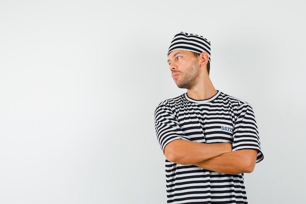 Young male in striped t-shirt hat looking aside with crossed arms and looking focused  