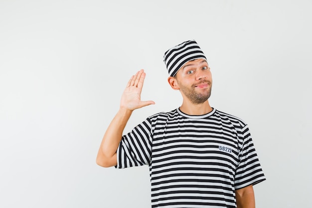 Young male in striped t-shirt hat waving hand for greeting and looking cheery  