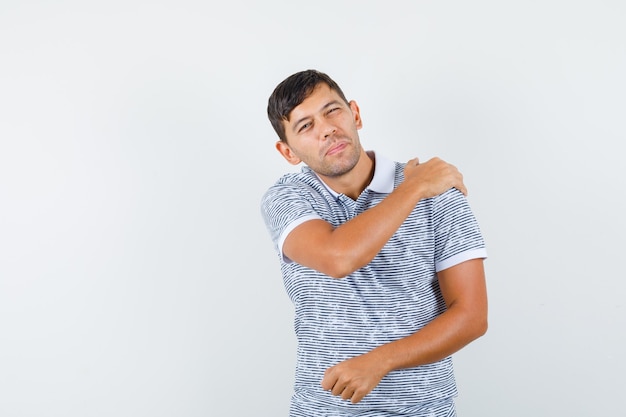 Young male suffering from shoulder pain in t-shirt and looking tired