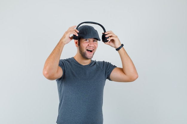 Young male in t-shirt cap wearing headphones and looking jolly  