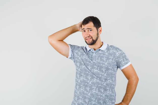 Young male in t-shirt holding hand on neck and looking elegant , front view.