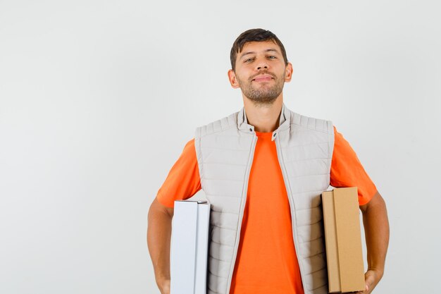 Young male in t-shirt, jacket holding cardboard boxes and smiling , front view.