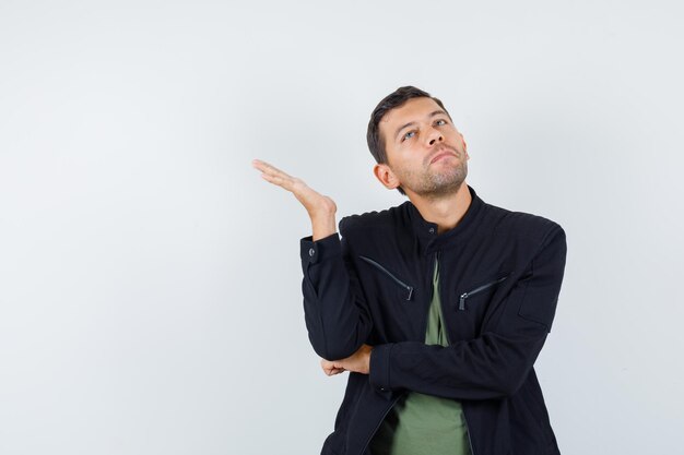 Young male in t-shirt, jacket looking up with raised palm and looking irritated , front view.