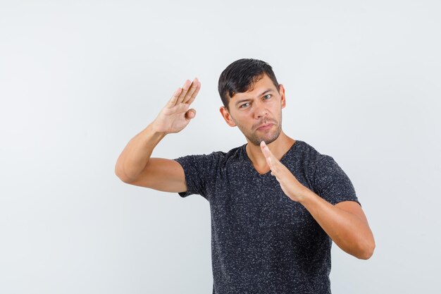 Young male in t-shirt showing karate chop gesture and looking confident , front view.