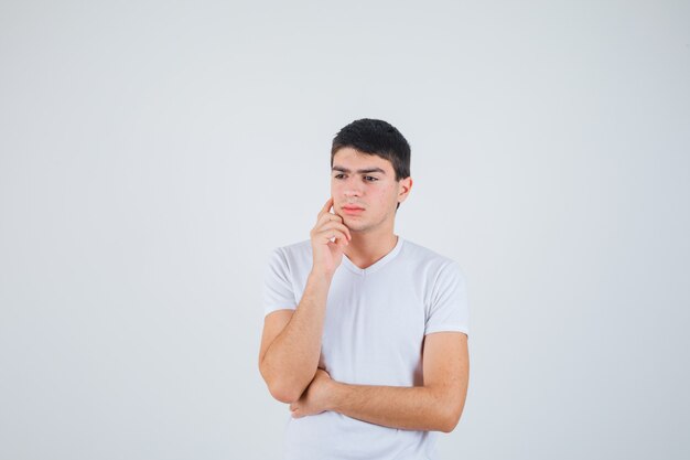 Young male in t-shirt standing in thinking pose and looking thoughtful , front view.