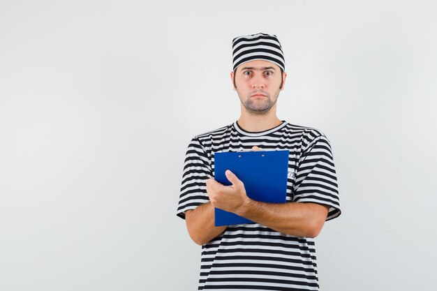 Free Photo young male taking notes on clipboard in t-shirt, hat and looking puzzled. front view.