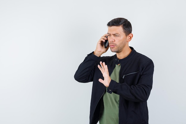 Young male talking on mobile phone with stop gesture in t-shirt, jacket front view.