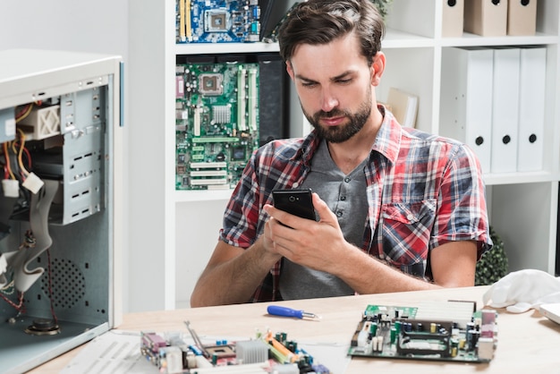 Young male technician using mobile phone in workshop