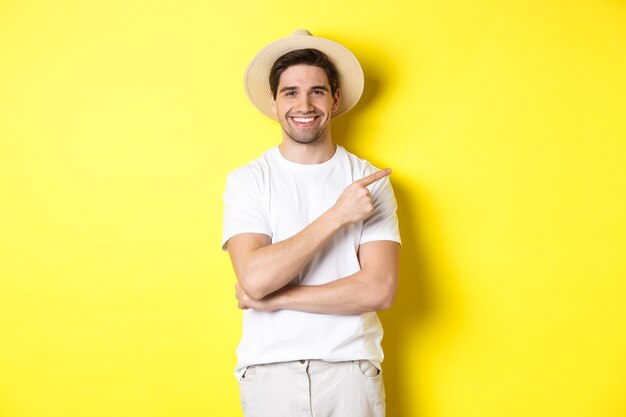 Young male tourist pointing finger right, smiling and showing advertisement, concept of tourism and lifestyle, yellow background.