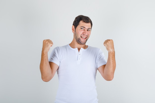 Young male in white t-shirt clenching fists and smiling and looking happy