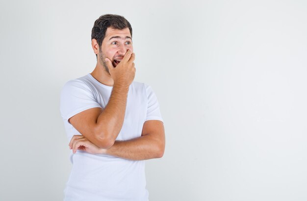 Young male in white t-shirt laughing with hand on mouth and looking happy