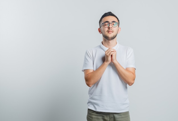 Free Photo young male in white t-shirt, pants clasping hands in praying gesture and looking hopeful