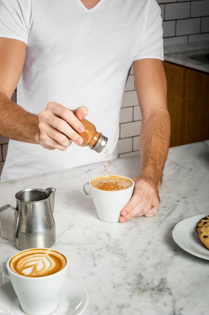 Young man adding cinnamon into a cup of cappuccino