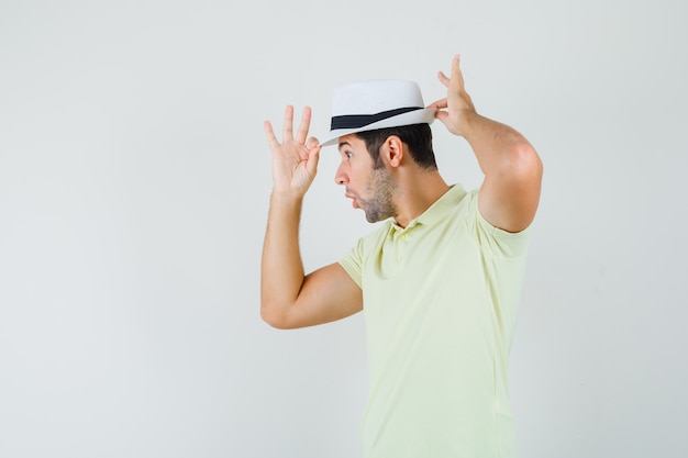 Free photo young man adjusting his hat in t-shirt and looking surprised