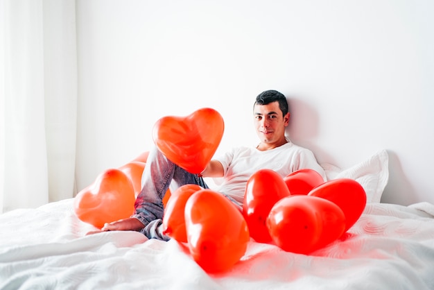 Free photo young man on bed between balloons in form of hearts