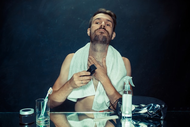 The young man in bedroom sitting in front of the mirror scratching his beard at home. Human emotions concept