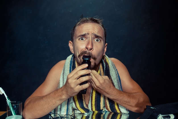 The young man in bedroom sitting in front of the mirror scratching his beard at home. Human emotions and lifestyle concept