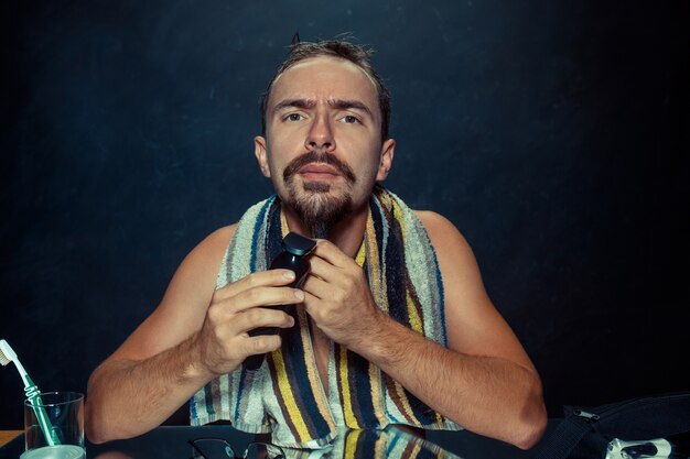 young man in bedroom sitting in front of mirror scratching his beard at home