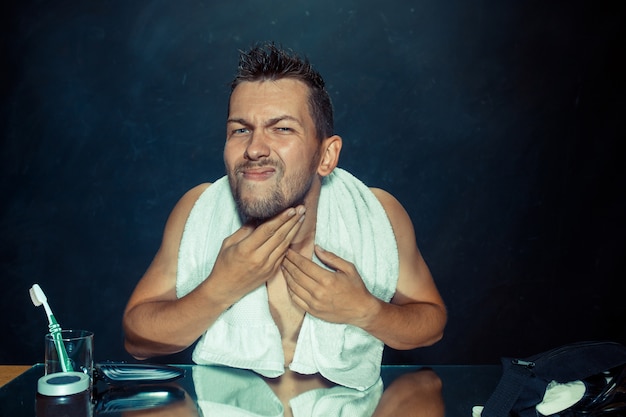 Free Photo young man in bedroom sitting in front of mirror scratching his beard at home