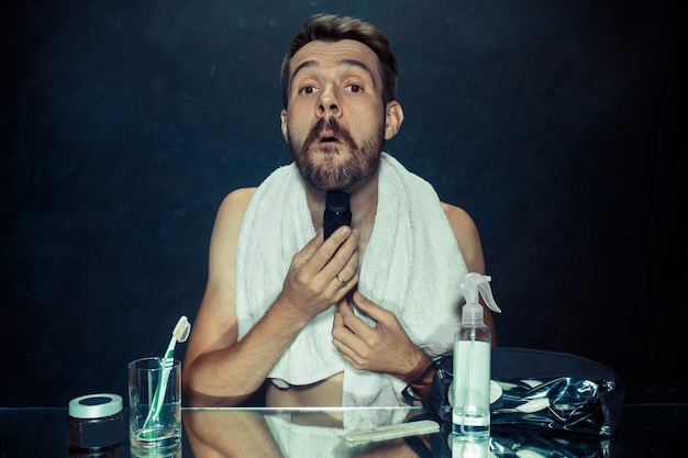 Free Photo the young man in bedroom sitting in front of the mirror scratching his beard at home