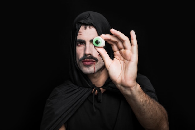 Free photo young man in black cloak with hood showing artificial eye