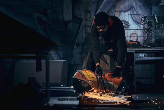 Young man in black gloves polishing metal in dark room