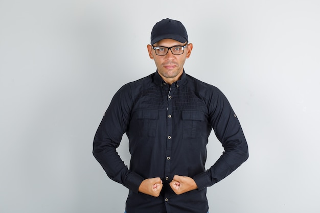 Free photo young man in black shirt with cap, glasses clenching his fists and looking confident