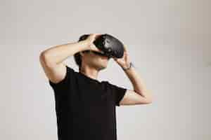 Free photo a young man in blank black t-shirt puts on vr glasses isolated on white