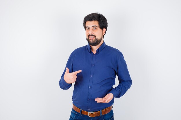 Young man in blue shirt and jeans stretching hand as holding something and pointing at himself and looking optimistic , front view.