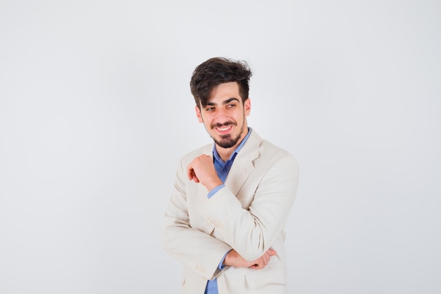 Young man in blue shirt and white suit jacket standing in thinking pose and looking happy