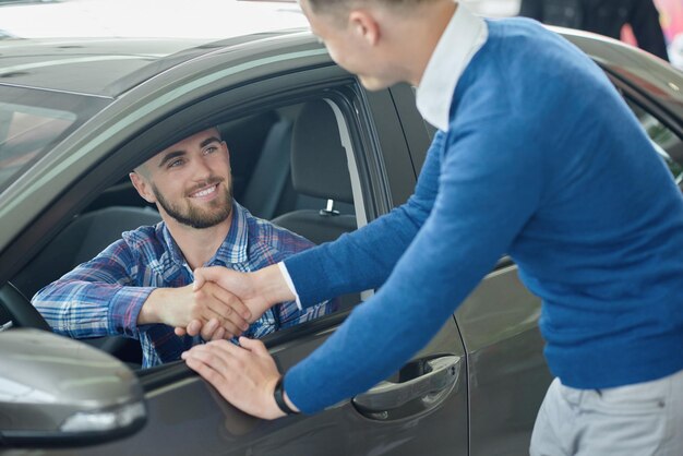 Young man in blue sweater helping friend choosing vehicle