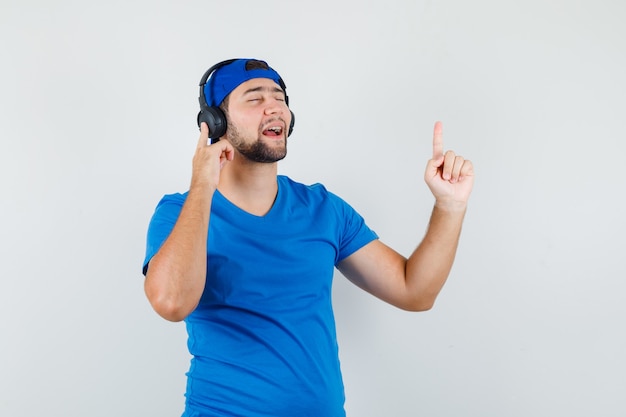 Young man in blue t-shirt and cap enjoying music with headphones with finger up